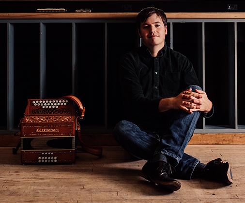 Will Pound sitting on wooden floor next to his melodeon